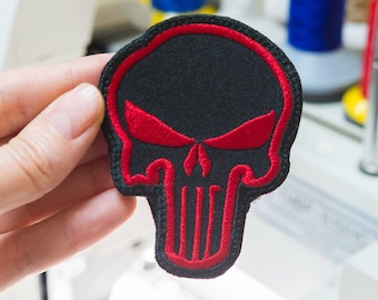 May include: A black and red embroidered skull patch with a red outline. The skull has a red nose and eyes.