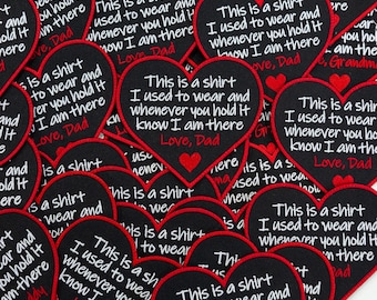 May include: A collection of heart-shaped fabric patches with black backgrounds and red borders. Each patch features white embroidered text that reads: This is a shirt I used to wear and whenever you hold it know I am there. Love, Dad or Grandma.
