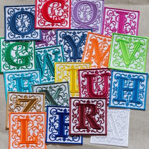 May include: A set of 16 colorful embroidered fabric patches featuring the letters of the alphabet in a decorative font. Each patch is square and has a white background with a decorative border.