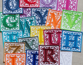 May include: A set of 16 colourful embroidered fabric patches featuring the letters of the alphabet in a decorative font. Each patch is square and has a white background with a decorative border.