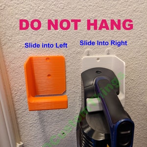 May include: A white wall mount with the text "DO NOT HANG" in pink letters. The wall mount is designed to hold a cordless vacuum cleaner. The vacuum cleaner is blue and black and is partially visible in the image. The text "Slide into Left" and "Slide into Right" are written in blue letters below the wall mount.