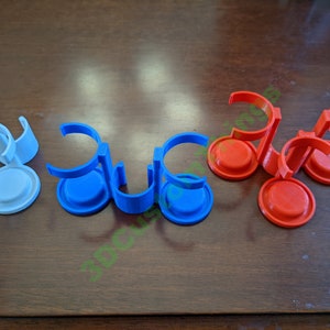 Puede incluir: Tres soportes para botellas impresos en 3D, uno blanco, uno azul y uno rojo. Cada soporte tiene tres bucles para botellas y una base circular.