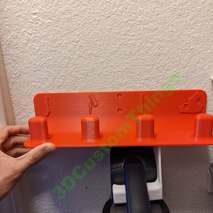 May include: A 3D printed orange wall mount with four slots for holding tools or accessories. A black and blue cordless vacuum cleaner is attached to the mount.