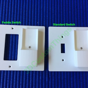 May include: Two white plastic wall plates for electrical outlets. The plate on the left is labeled "Paddle Switch" and the plate on the right is labeled "Standard Switch". Both plates have a rectangular cutout for a switch and a small rectangular cutout on the right side.