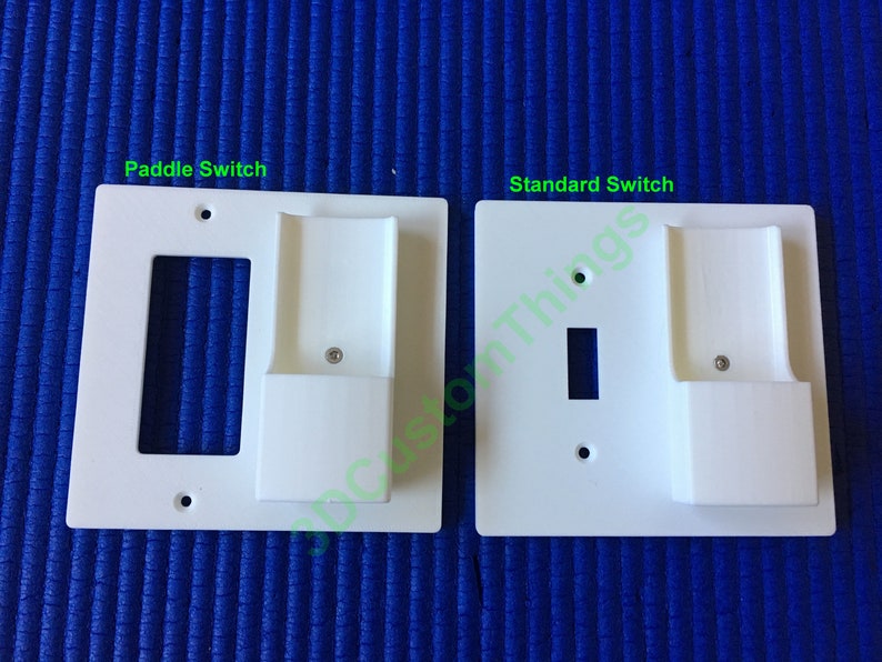 May include: Two white plastic wall plates for electrical outlets. The plate on the left is labeled "Paddle Switch" and the plate on the right is labeled "Standard Switch". Both plates have a rectangular cutout for a switch and a small rectangular cutout on the right side.