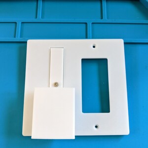 May include: White plastic wall plate with two rectangular openings. One opening is for a light switch and the other is for a standard outlet.