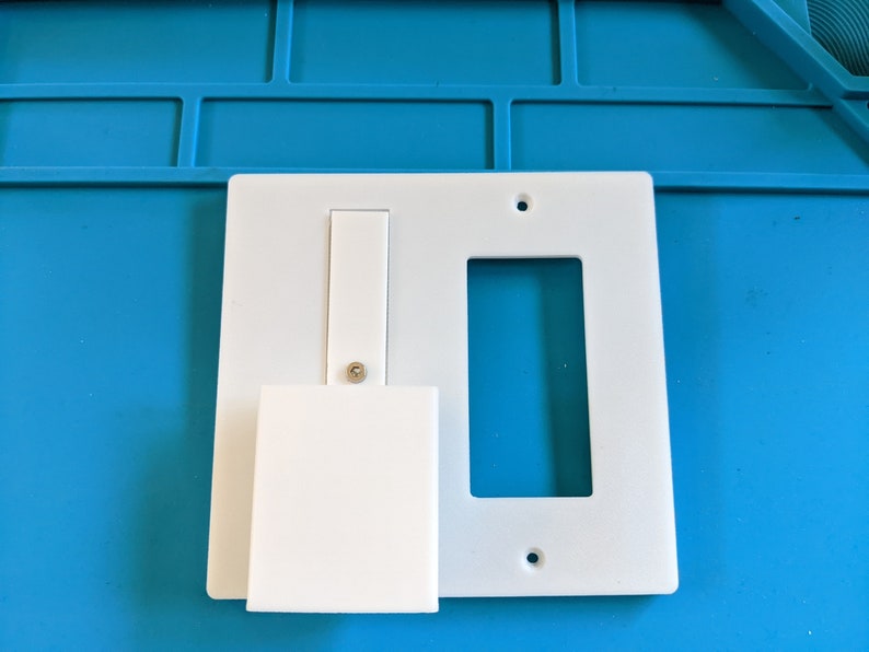 May include: White plastic wall plate with two rectangular openings. One opening is for a light switch and the other is for a standard outlet.