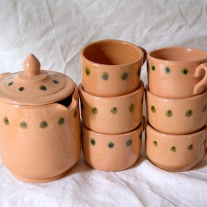 Peut inclure: Ensemble de vaisselle en céramique pêche faite à la main, comprenant un sucrier avec couvercle et six tasses et bols. Chaque pièce est ornée de petits pois verts espacés, créant une esthétique rustique et charmante.