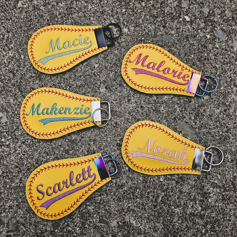 May include: Five yellow baseball-shaped keyrings with embroidered names: Macie, Malorie, Mackenzie, Narah, and Scarlett. Each keyring has a silver metal ring.