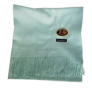 Peut inclure: Une écharpe en cachemire bleu clair avec des franges. L'écharpe porte une étiquette noire indiquant "Cachemire" et une étiquette noire et or indiquant "B-Vito".