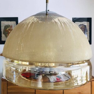 May include: A gold and clear glass dome pendant light fixture with a textured, frosted glass top and a clear glass bottom. The light fixture has a brushed metal top.
