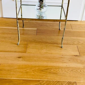 May include: A gold metal two-tiered serving cart with mirrored shelves. The cart has a floral arrangement with red flowers in a clear glass vase on the lower shelf. Two white teacups with floral patterns are on the top shelf.