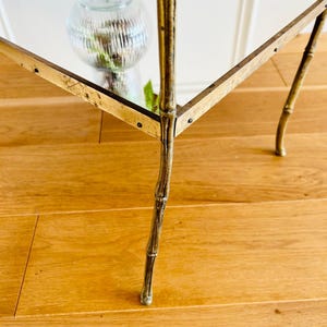 May include: A gold-toned mirrored side table with a bamboo-style base. The table has a square top and four legs.