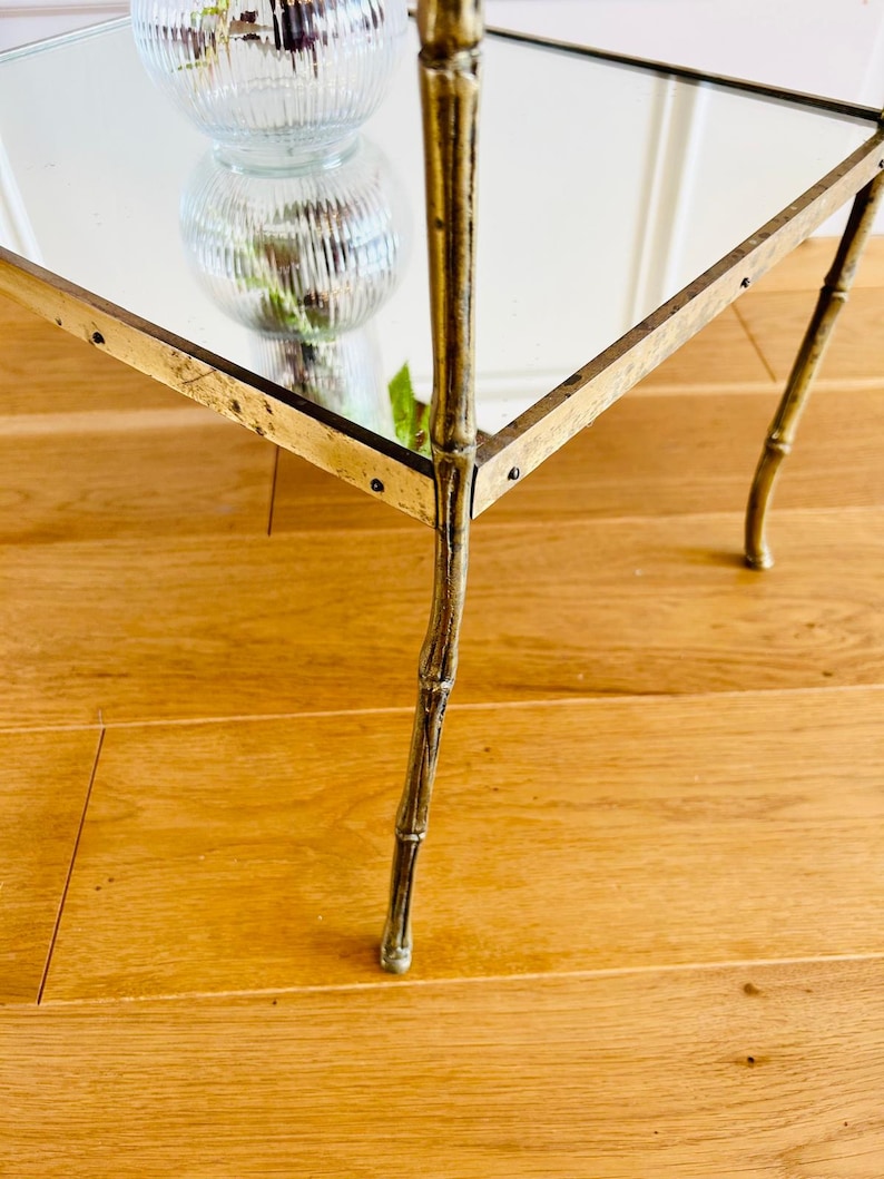 May include: A gold-toned mirrored side table with a bamboo-style base. The table has a square top and four legs.