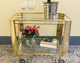 A rare Art Deco 1930s golden bar cart made of brass with two tiers of glass on rubber wheels.