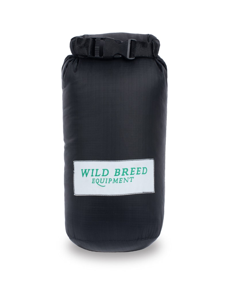 May include: Black dry bag with a black strap and buckle. The bag has a white label with green text that reads "WILD BREED EQUIPMENT".