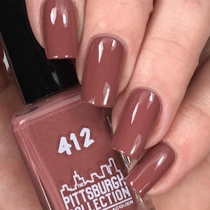 May include: A close-up of a hand with polished nails in a mauve color. The nail polish bottle is visible, displaying the number "412" and the text "The Pittsburgh Collection by Gridlock Lacquer". The nails are a glossy, solid color.
