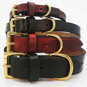 May include: Four leather dog collars in different sizes, stacked on top of each other. The collars are brown, black, and burgundy with gold metal buckles.