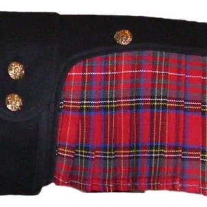 May include: A black fabric garment featuring a pleated section with a red, blue, and yellow tartan plaid pattern. The black portion includes a vertical strap secured by two round, textured gold-tone metal buttons, with two additional matching buttons along the top edge of the plaid fabric.