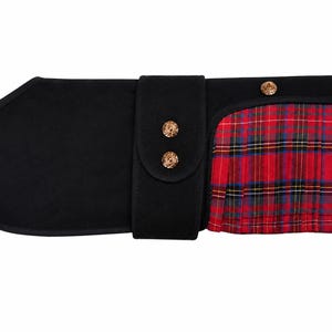 May include: A black pet coat featuring a solid black main body with a central vertical strap secured by two gold-toned metal buttons. The right side displays a pleated red, blue, and yellow plaid fabric panel accented with two additional gold-toned buttons.