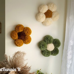 May include: Three handmade pom-pom flower wall decorations in yellow, white, and green. The flowers are made of yarn and have a center circle of a different color.
