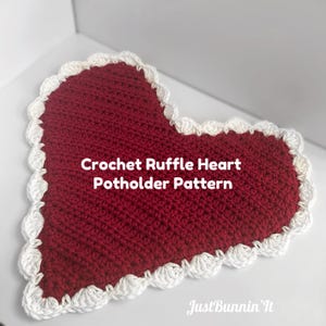 May include: A heart-shaped, red crochet potholder with a white ruffled edge. The text "Crochet Ruffle Heart Potholder Pattern" is displayed on the potholder. The potholder is handmade and likely used in the kitchen.