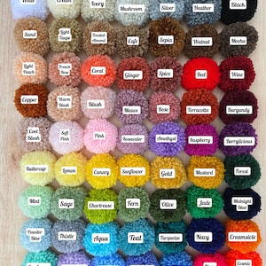 May include: A color palette of 49 yarn pom-poms in various colors, arranged in a grid. The pom-poms are labeled with names like "White", "Cream", "Ivory", "Black", "Sand", "Light Taupe", "Toasted Almond", "Cafe", "Sepia", "Walnut", "Mocha", "Light Peach", "French Rose", "Coral", "Ginger", "Spice", "Red", "Wine", "Copper", "Warm Blush", "Blush", "Mauve", "Rose", "Terracotta", "Burgundy", "Cool Blush", "Soft Pink", "Pink", "Rosewater", "Amethyst", "Raspberry", "Berrylicious", "Buttercup", "Lemon", "Canary", "Sunflower", "Gold", "Mustard", "Forest", "Mint", "Sage", "Chartreuse", "Fern", "Olive", "Jade", "Midnight Blue", "Powder Blue", "Thistle", "Aqua", "Teal", "Turquoise", "Navy", "Creamsicle", "Seafoam", "Lavender", "Bluebell", "Periwinkle", "Cornflower", "Neon Pink", "Cosmic Orange". The image includes the text "Color Palette" and "Just Bunnin' It".