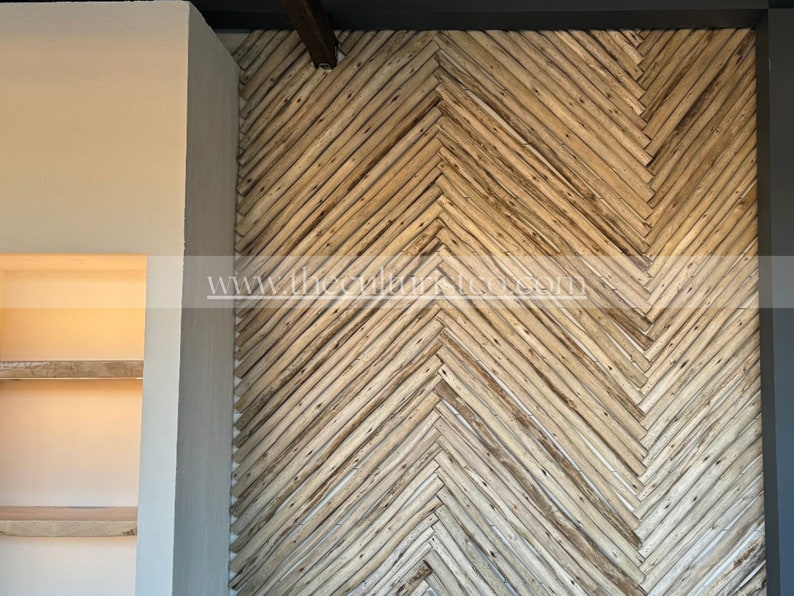 May include: A wall with a herringbone pattern made of light brown wooden planks. The planks are arranged diagonally, creating a textured surface. The wall is part of an interior design, with a neutral-colored wall and a dark gray border.
