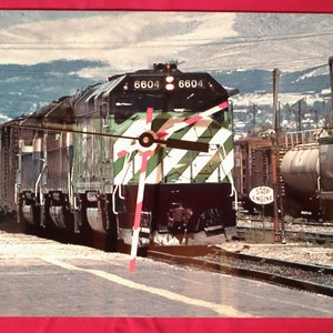 May include: A green and white striped train engine with the number 6604 on the side. The train is stopped on a set of tracks with a "Stop Engine" sign visible in the background.