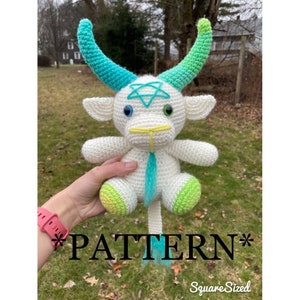 Puede incluir: Cabra de amigurumi de crochet blanco con cuernos verdes y azules, un pentagrama en la frente y detalles verdes y amarillos en las pezuñas. La cabra está sentada en la mano de una persona. El texto "*PATTERN*" es visible en la parte inferior de la imagen.