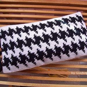 Puede incluir: Una bolsa de embrague de crochet en blanco y negro con un patrón de pata de gallo. La bolsa tiene una correa negra y está sobre una superficie de madera.