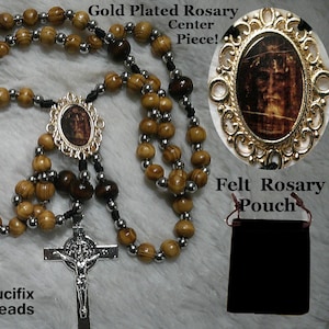 May include: A wooden rosary with a gold-plated centre piece featuring an image of the Shroud of Turin. The rosary is made with dark brown and light brown wooden beads and silver spacer beads. It comes with a black felt pouch. "Shroud Of Turin! HOLY FACE ROSARY Made By MICHAELSCAPULARS £20 With Strong SGT Rosary Cord Wooden Beads Larger Dark Brown Our Father Beads St Benedict Jubilee Medal Crucifix With Stainless Steel Spacer Beads Felt Rosary Pouch"