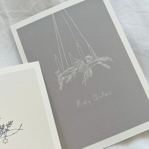 May include: A gray card with a white line drawing of a candle chandelier with greenery hanging from it. The text "Merry Christmas" is written in white below the drawing.
