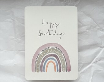 May include: A white card with the text "Happy Birthday" in black script. A rainbow with purple, blue, and orange stripes is drawn below the text.