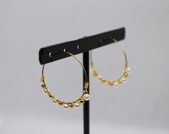 May include: Gold hoop earrings with small white pearls hanging from the hoops.