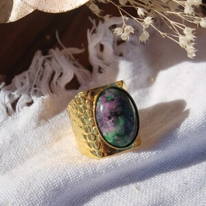 Peut inclure: Une bague en or avec une grande pierre ovale verte et rose sertie au centre. La bague a une bande texturée.