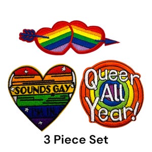 Peut inclure: Un ensemble de trois écussons brodés aux couleurs de l'arc-en-ciel. L'un représente deux cœurs percés d'une flèche. Un autre, en forme de cœur, dit "SOUNDS GAY I'M IN". Le troisième dit "Queer All Year!"