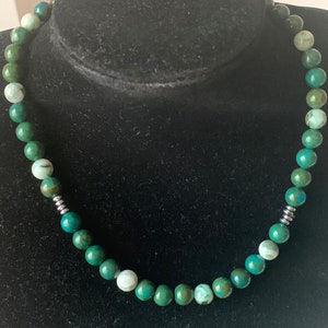 May include: A green and white gemstone beaded necklace with silver accents. The necklace is made of round beads and is approximately 18 inches long.
