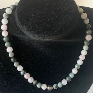 Puede incluir: Un collar hecho de cuentas de piedras preciosas rosas y verdes con un cierre de metal plateado.