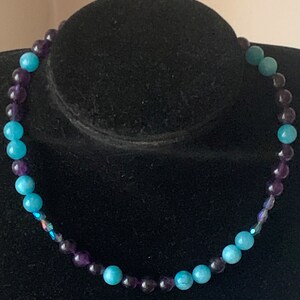 Puede incluir: Un collar hecho con cuentas redondas alternando azul claro y morado. Las cuentas son lisas.