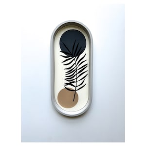 May include: A white oval tray with a black and brown abstract design. The design features a stylized leaf with a black circle and a brown circle behind it.