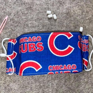 May include: A blue and red face mask with the text "CHICAGO CUBS" and a red "C" on a blue background. The mask has white elastic straps.