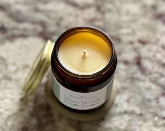 May include: A brown glass jar candle with a white label that reads "Blue Wild Botanicals, Soy & Tallow Candle, Lavender Eucalyptus". The candle is lit and the wax is a light yellow color.