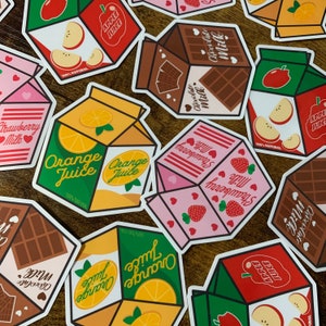 May include: A collection of colorful juice box designs. The designs include orange juice, strawberry milk, chocolate milk, and apple juice. The boxes are all made of cardboard and have a variety of illustrations and text. The text on the boxes includes 