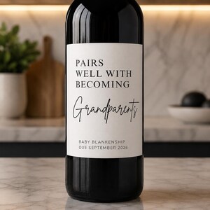 Op de afbeelding: Een donkere wijnfles met een wit etiket. Het etiket leest "PAIRS WELL WITH BECOMING Grandparents" in een scriptlettertype. De tekst "BABY BLANKENSHIP DUE SEPTEMBER 2026" is ook zichtbaar.