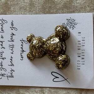 Peut inclure: Épingle en forme d'ours en paillettes dorées sur une carte blanche avec du texte manuscrit. La carte indique "Si vous vous sentez triste ou seul, cet ours vous tiendra compagnie" et "Gardez-moi près de vous, je suis toujours là."