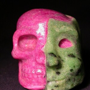 May include: A pink and green gemstone skull sculpture. The skull is carved from two different types of gemstones, one pink and one green.