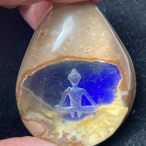 以下が含まれることがあります： 穏やかな瞑想の姿が描かれた、涙型のペンダント。ペンダントは、青と黄色の背景と透明な外層を持つ多層設計です。その姿は、座ったヨガのポーズをとっています。