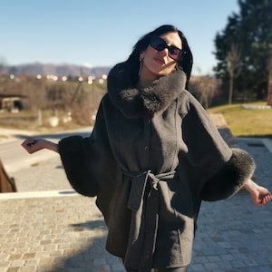May include: A grey wool cape with a black fur collar and cuffs. The cape has a belt and a button fastening.
