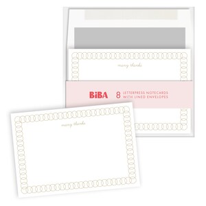 May include: A set of eight white letterpress notecards with a gold circular chain border and the text "many thanks" in script. The cards are packaged in a clear sleeve with a pink band labeled "BiBA 8 LETTERPRESS NOTECARDS WITH LINED ENVELOPES."